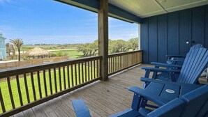 A covered outdoor deck with wooden flooring and blue Adirondack chairs.