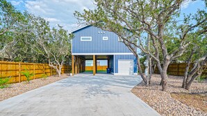 A two-story building with a garage, surrounded by a wooden fence and trees.
