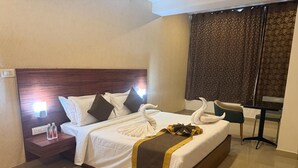 A hotel room with a bed, a nightstand, a chair, a table, and a curtain. - Aero Hotel Near Bangalore International Airport (Bengaluru)