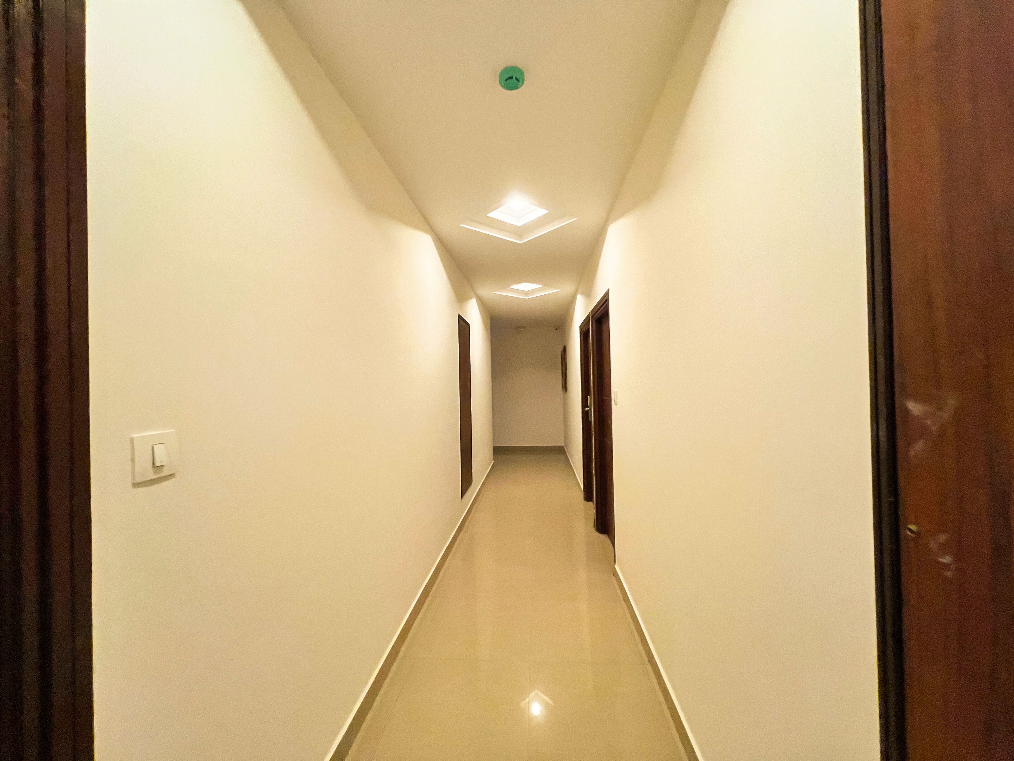 A narrow, well-lit hallway with white walls and a wooden door on the right.
