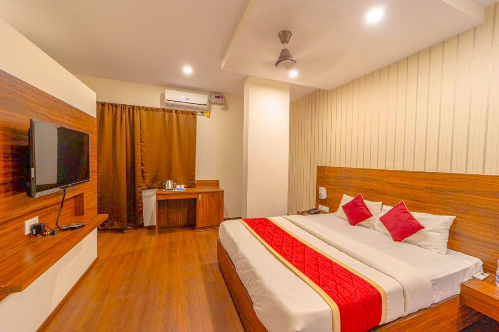 A hotel room with a wooden bed, a desk, a television, and an air conditioning unit.