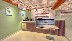 A modern cafe interior with a counter, menu board, and air conditioning unit. - Aero Hotel Near Bangalore International Airport (Bengaluru)
