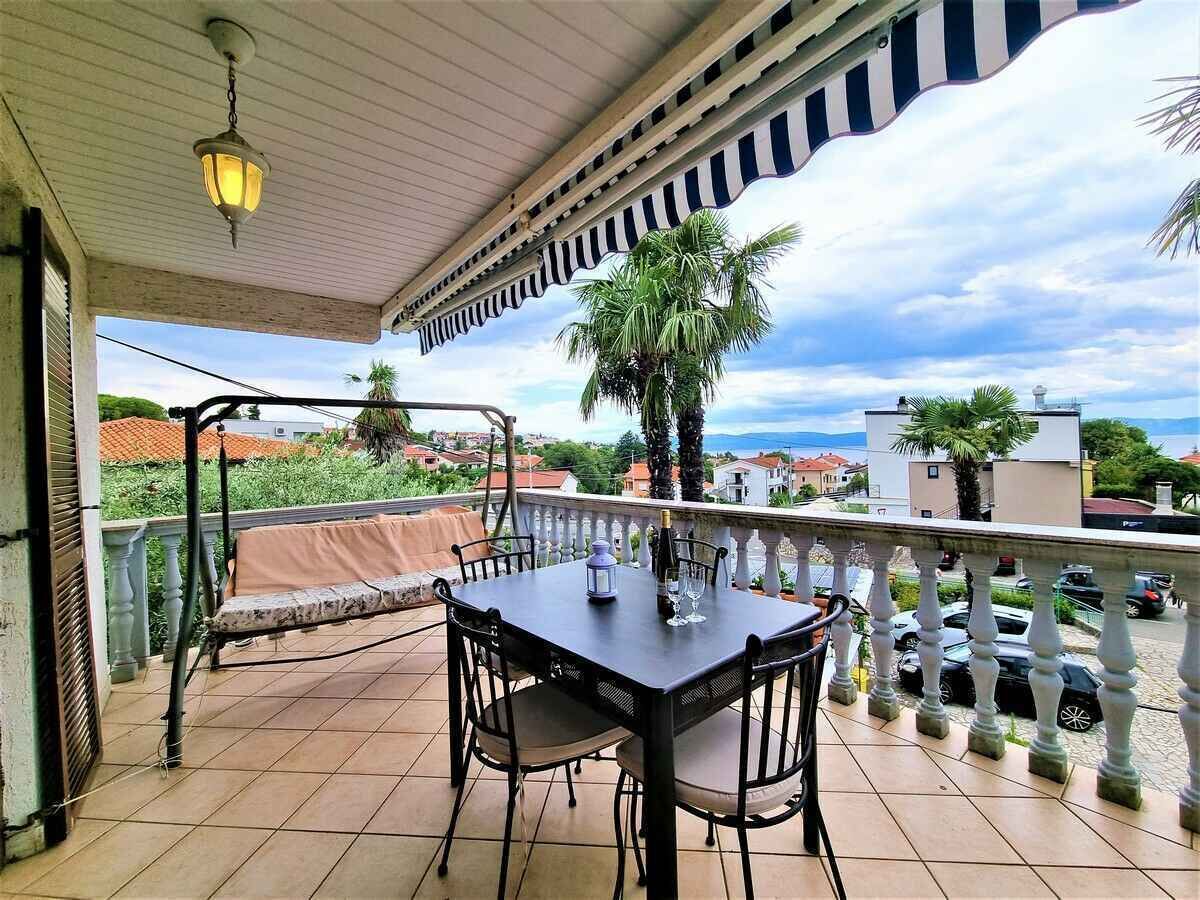 A balcony with a table and chairs, a hanging light fixture, and a view of the sea and buildings.