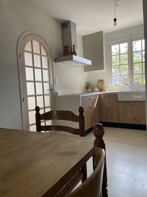 Een keuken met een houten tafel en stoelen, een raam met uitzicht op bomen, en een inbouwfornuis.