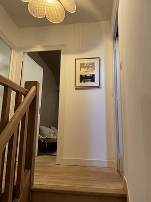Een trap met een houten leuning die naar een slaapkamer leidt. Daarboven, aan de muur, hangt een lijst met een kunstwerk.