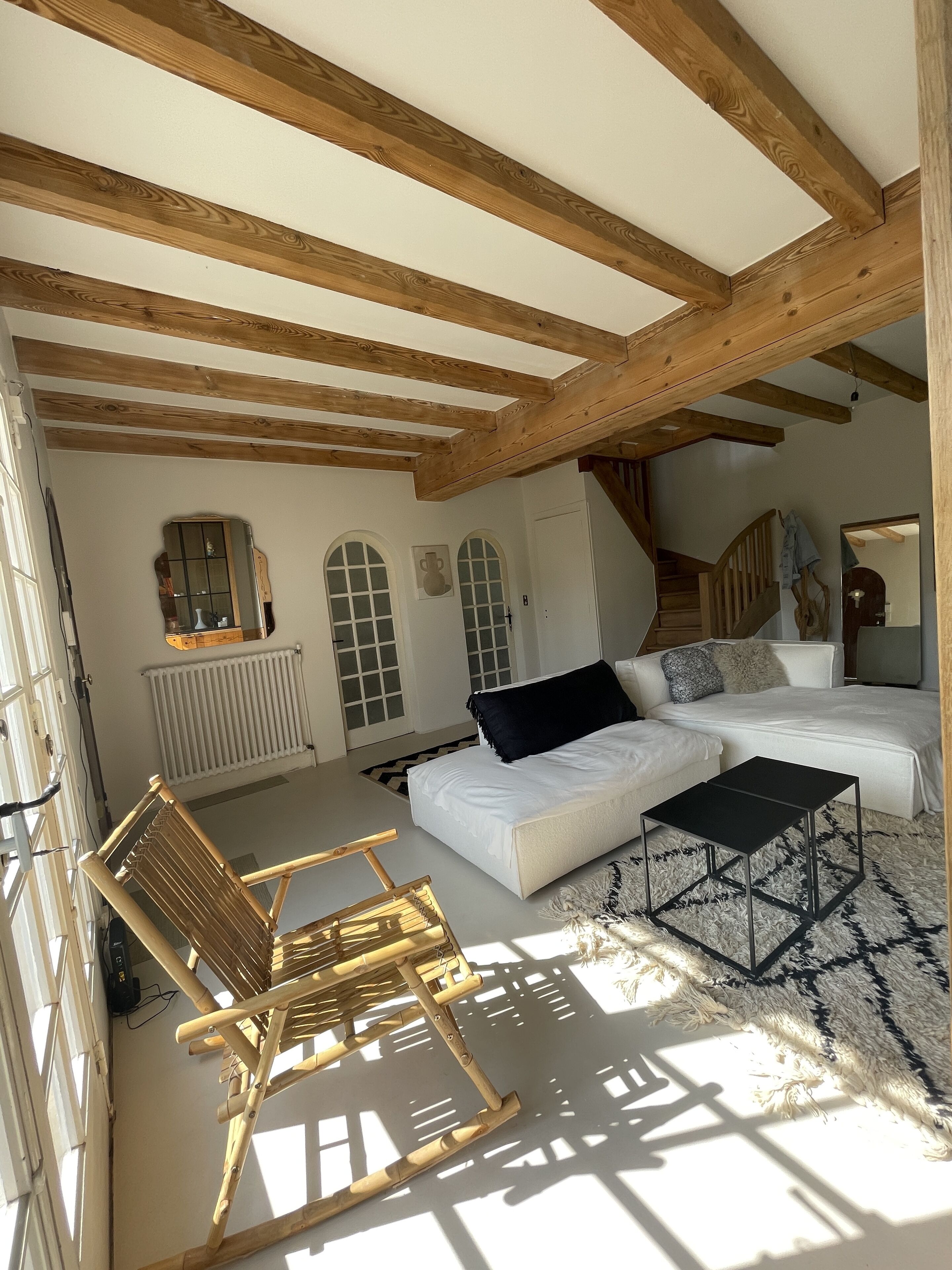 A cozy living room with a wooden ceiling, a white sofa, a black coffee table, and a wooden rocking chair.