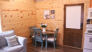Une pièce chaleureuse avec un décor intérieur en bois, une table à manger avec des chaises, un canapé et un poêle blanc.