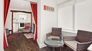 Una habitación acogedora con mobiliario de mimbre, una mesa de vidrio y vistas a una cocina a través de una puerta abierta.