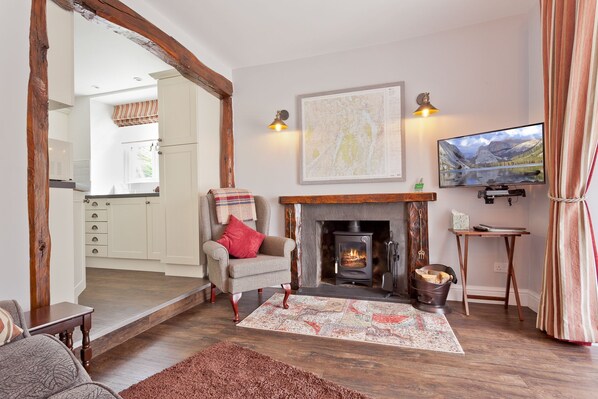 A cozy living room with a fireplace, a television, and a kitchen in the background. - Mole's Cottage, beautiful cottage overlooking Coniston Water (Coniston)