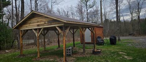 Une cabane en bois avec un toit en pente, une petite véranda et un foyer extérieur.