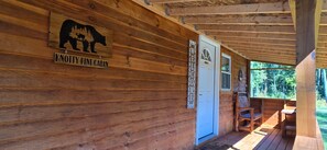 Een houten chalet met een berenlogo en een bord met de tekst 'Knottty Pine Cabin', een welkomstbord en een houten bank.