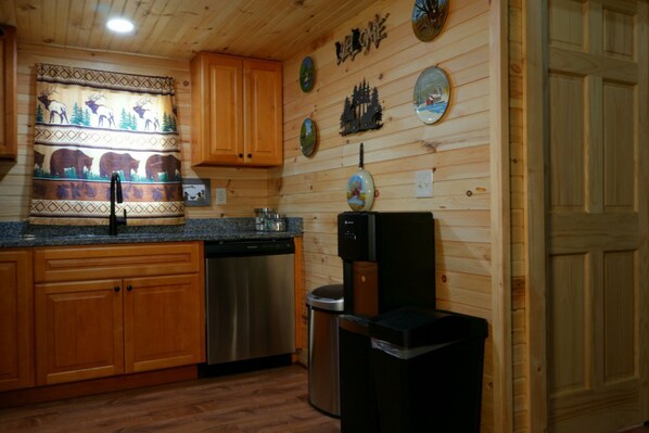 A kitchen with wooden cabinets, a stainless steel dishwasher, a water dispenser, and decorative plates on the wall.