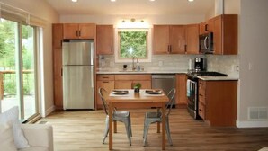 Une cuisine moderne dotée de meubles en bois, d’appareils électroménagers en acier inoxydable et d’un coin repas avec une table et des chaises.