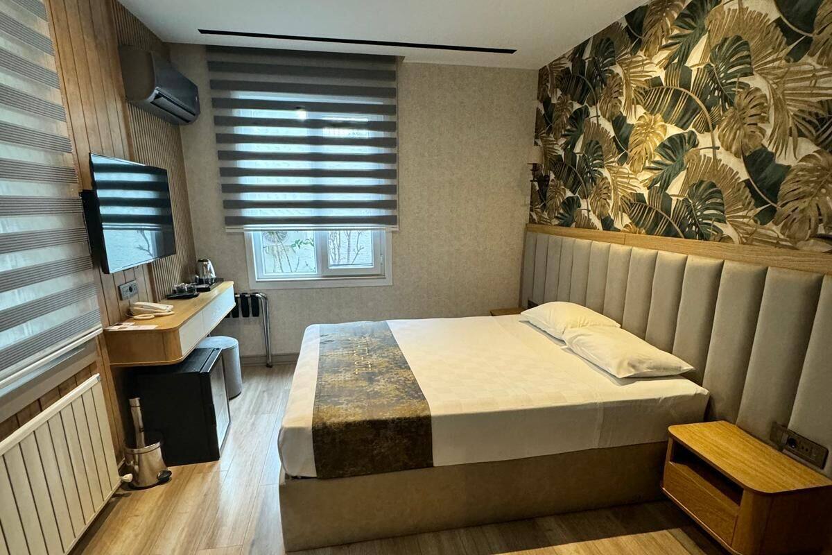 A modern bedroom with a large bed, a TV, a desk, and a window with blinds.
