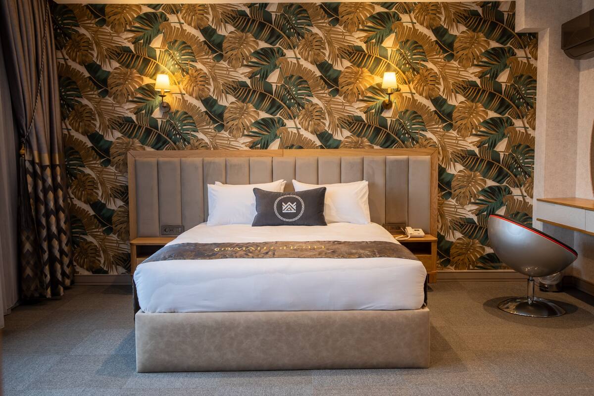 A neatly made bed with a headboard, a bedside table with a lamp, and a modern chair.