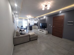 A modern living room with a sofa, TV, and kitchen in the background. - San Pawl Lodge (St. Paul's Bay)