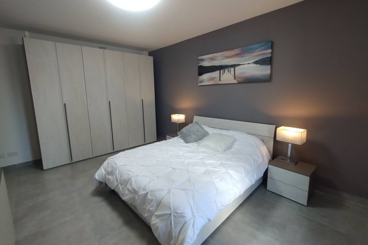 Ein Schlafzimmer mit einem Bett, Nachttischen, einem Gemälde und einem Kleiderschrank.