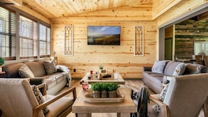 A cozy wooden interior with a large window, a central table with plants, and a sofa.