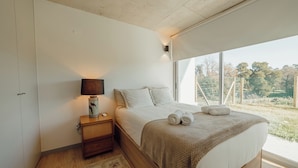 A bedroom with a large bed, a bedside lamp, a nightstand, and a view of a fenced outdoor area. - Amazing Design Garden by Vacationy (Vila Nova de Gaia)