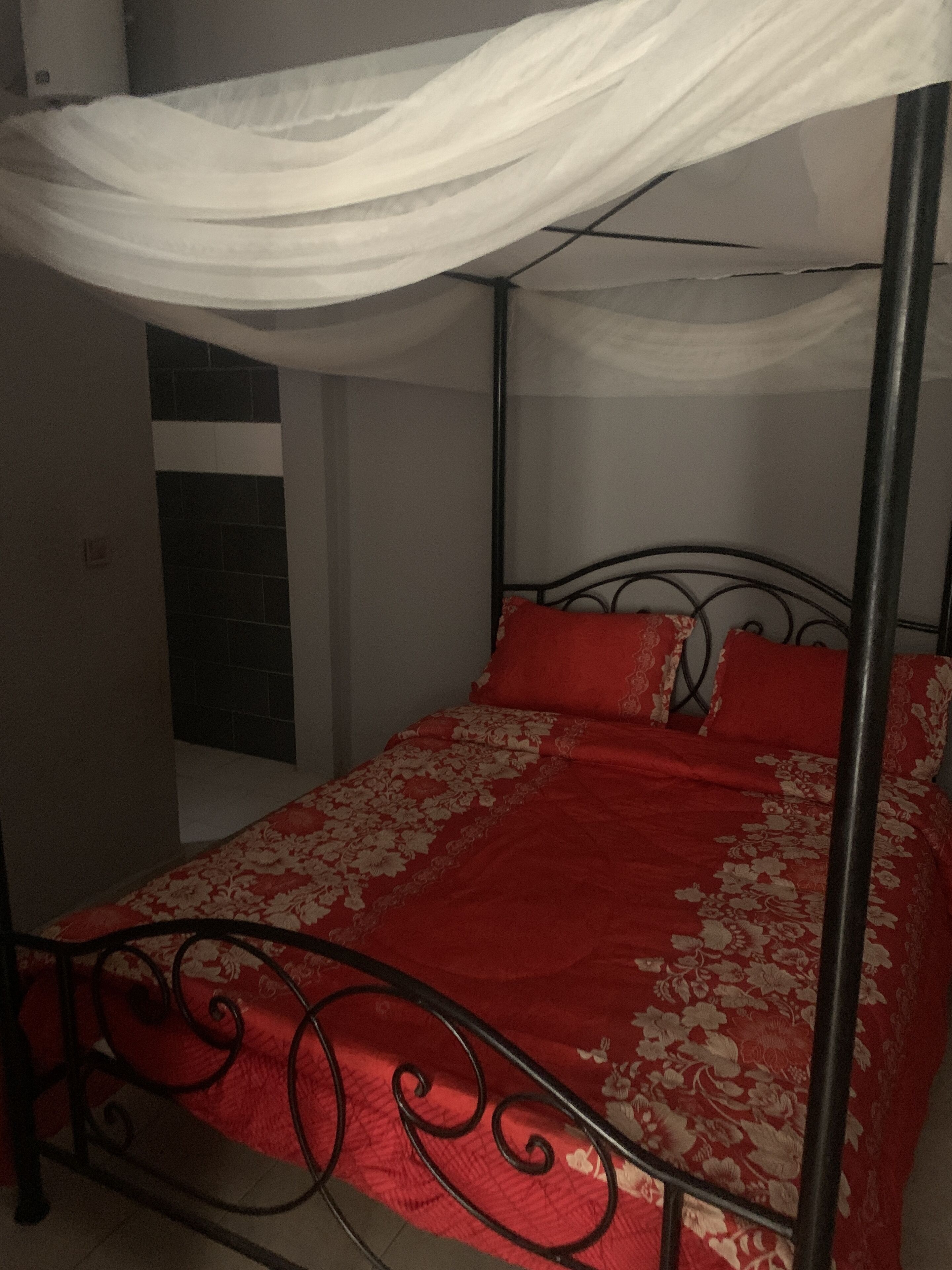 Un lit à baldaquin avec des rideaux, une literie rouge et une structure en métal noir.