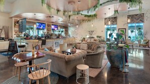 Una cafetería amplia con asientos cómodos, una zona de bar y un gran ventanal que proporciona luz natural.