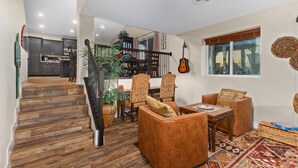 Een ruime woonkamer met een houten trap, een eetgedeelte met gestreepte stoelen, en uitzicht op de keuken en eetkamer door een glazen wand.