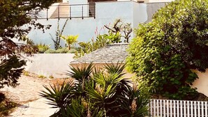 Ein modernes, zweistöckiges Haus mit Balkon, umgeben von üppiger Vegetation und einer Bergkulisse.