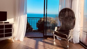 Ein Balkon mit Meerblick, ein Korbstuhl und ein Fernseher auf einem Schrank.