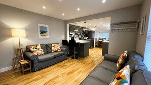 Un salon moderne avec un canapé gris, un plancher en bois et un coin cuisine à l’arrière-plan.