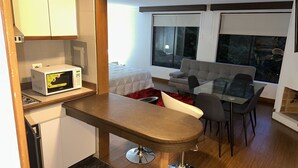 A compact living space with a kitchenette, a dining area with a glass table, a sofa, and a large window providing a view of the outdoors. - Departamento Amoblado Lloyd Apartment 94 (Bogotá)