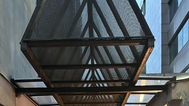 A covered walkway with a checkered tile pattern, leading to a building entrance with a glass door and a clock above it. - Departamento Amoblado Lloyd Apartment 94 (Bogotá)