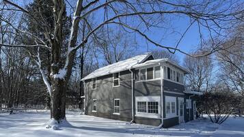 A two-story house with a snow-covered roof and a large tree in front.