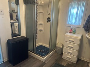 Un bagno compatto con doccia, un lavandino piccolo, uno specchio e un armadietto.