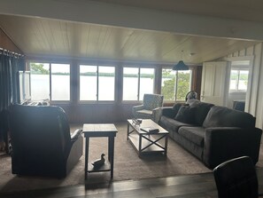A room with a large window, a sofa, a chair, a small table, and a fan.