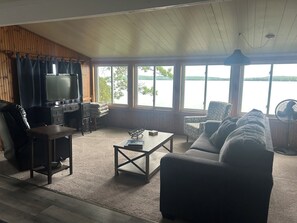 A living room with a television, sofa, coffee table, and large windows overlooking a body of water.