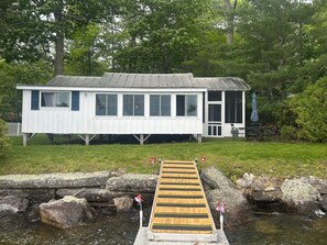 A cabin with a dock extending over a stream, surrounded by trees.