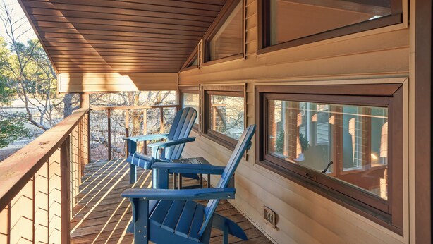 Eine Holzterrasse mit blauen Adirondack-Stühlen und großen Fenstern.