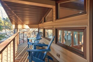 Une terrasse en bois avec des chaises Adirondack bleues et de grandes fenêtres.