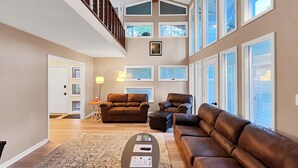 Ein geräumiges Wohnzimmer mit hoher Decke, großen Fenstern und einem Deckenventilator.