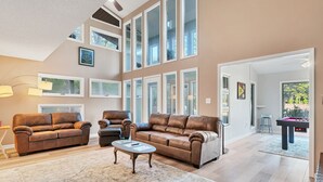 Ein geräumiges Wohnzimmer mit Ledersofas, einem Couchtisch und einem großen Fenster mit vielen Scheiben.