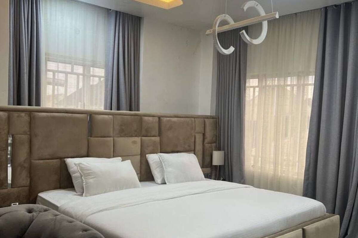 Une chambre moderne avec un grand lit, une tête de lit capitonnée et des rideaux gris.