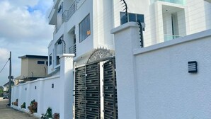 Un edificio residencial moderno de varios pisos, con fachada blanca, ventanas grandes y entrada protegida por una reja.