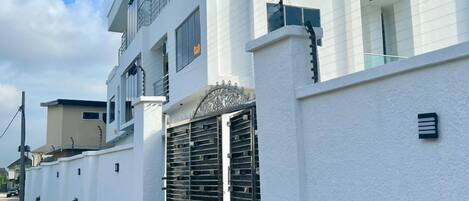 Un edificio residencial moderno de varios pisos, con fachada blanca, ventanas grandes y entrada protegida por una reja.