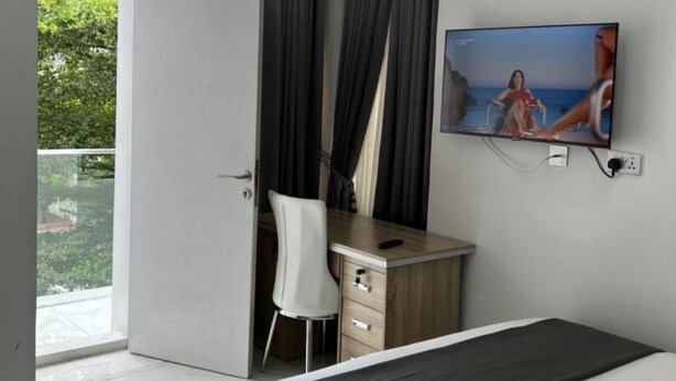 Un dormitorio moderno con cama, escritorio, silla, televisor y balcón.