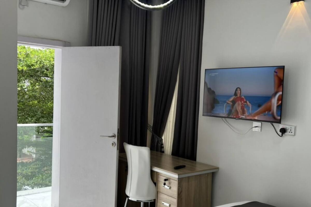 Une chambre moderne équipée d’un lit, d’un bureau, d’une chaise, d’une télévision et d’un balcon.
