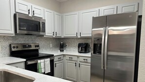 A kitchen with white cabinets, stainless steel appliances, and a herringbone tile backsplash.