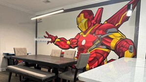 A dining area with a table and chairs, a bench, and a wall mural of a superhero.