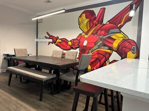 Zona pranzo con tavolo e sedie, una panca e un affresco raffigurante un supereroe.