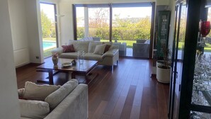 Un salón amplio con un sofá grande, una mesa de centro y un aparador de vidrio con copas de vino.