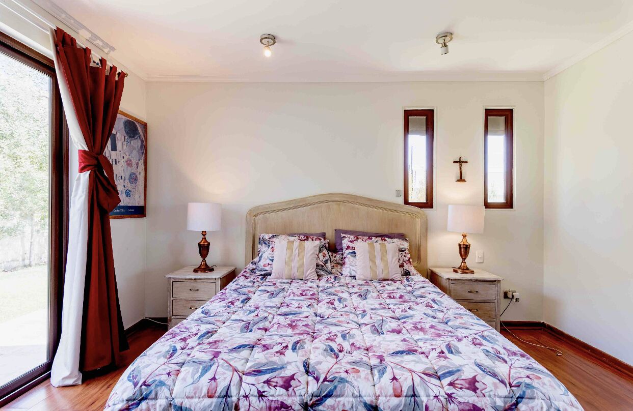 A bedroom with a large bed, two nightstands, a window with curtains, and a cross on the wall.